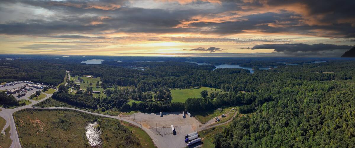 An aerial view of a forested landscape with a river, a parking lot, and a bridge.