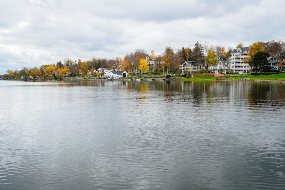 A calm lake with autumn-colored trees and residential buildings along the shore.