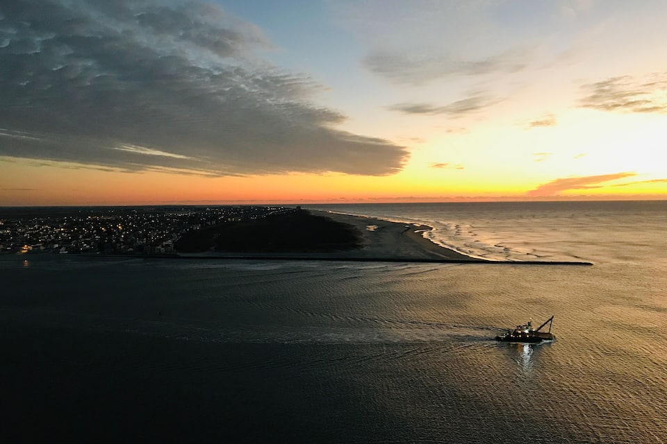 A coastal cityscape at sunset with a boat on the water.