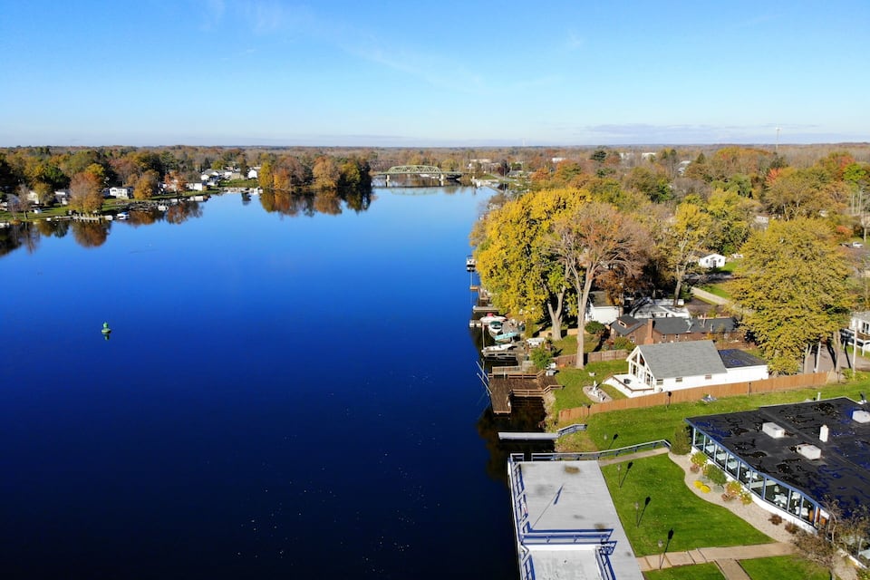 A calm lake with a dock, surrounded by autumn-colored trees and residential buildings.