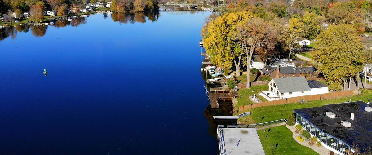 A calm lake with a dock, surrounded by autumn-colored trees and residential buildings.