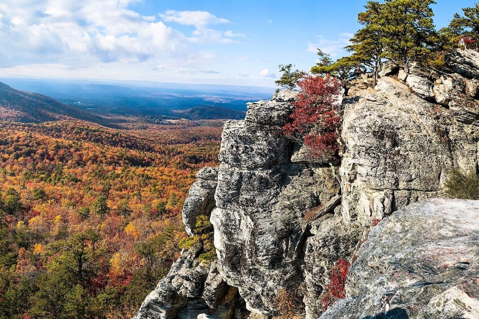 A mountainous landscape with autumn foliage, rocky cliffs, and a distant mountain peak.