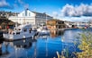 Een haven met aangemeerde boten, een museum en een gebouw aan het water.