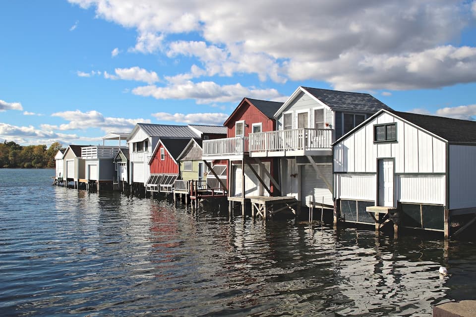 A row of waterfront houses with a lake and a partly cloudy sky.