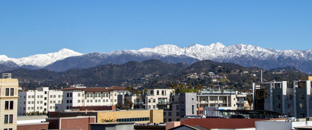 A cityscape with modern buildings and snow-capped mountains in the background.