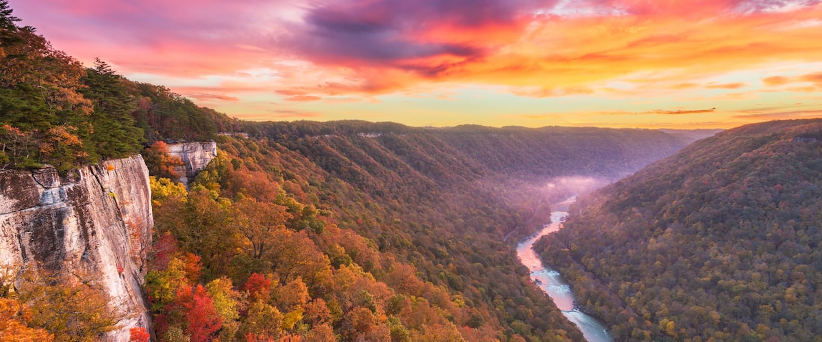 A canyon with a river, autumn foliage, and a rocky cliff.