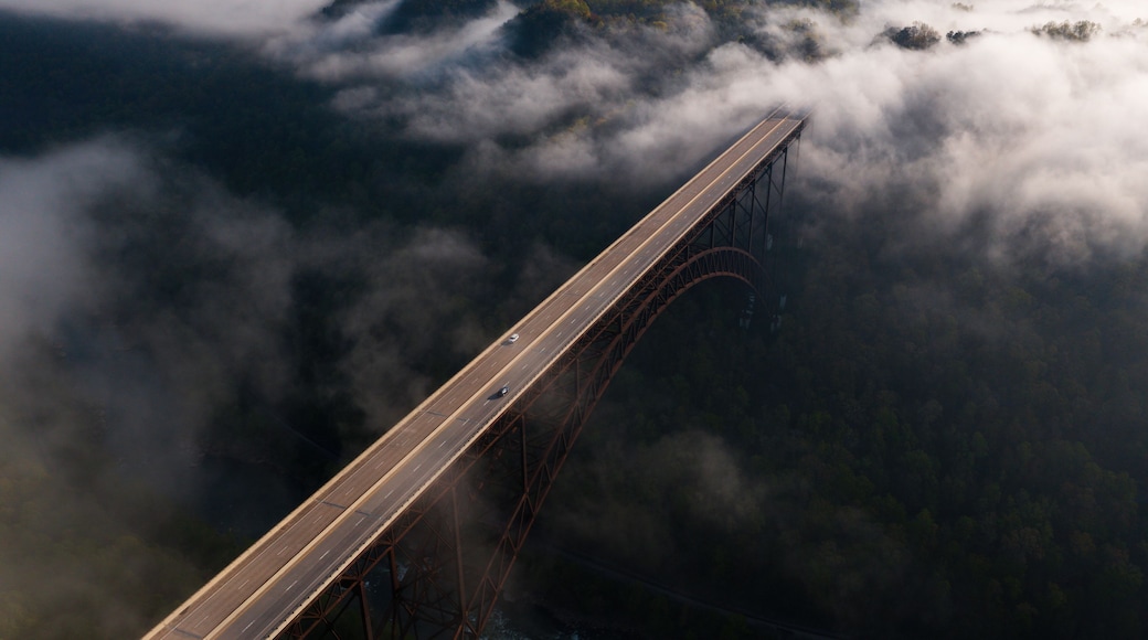 Eine Brücke mit Stahlkonstruktion und einer Straße, umgeben von Wolken und einer bewaldeten Landschaft.