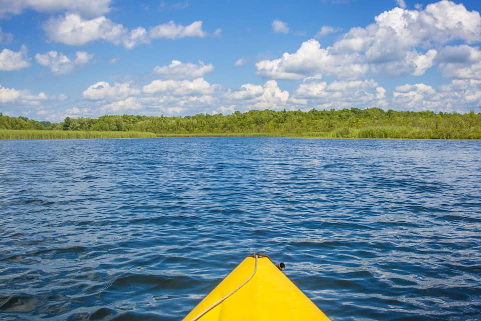 A yellow kayak on a calm lake with a forested shoreline under a partly cloudy sky.