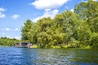 A lakeside house with a dock, surrounded by lush green trees and clear blue sky.