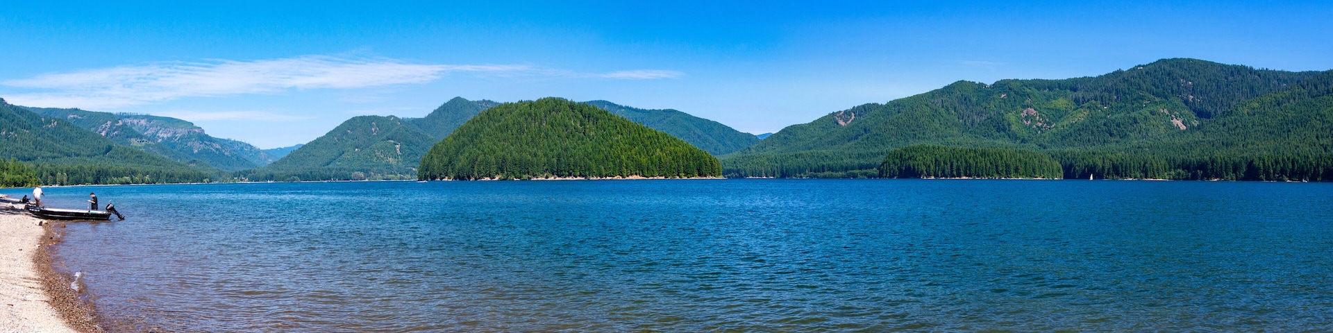 Scenic panorama of Detroit Lake, Oregon. Blue crystal clear water, sky with clouds small island in the middle and a fishing boat on a lake beach