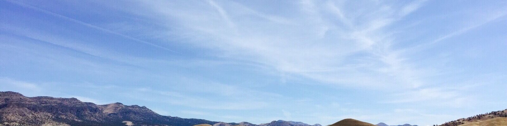 Uma pessoa sentada em uma colina, com vista para paisagens áridas coloridas e montanhas ao longe.