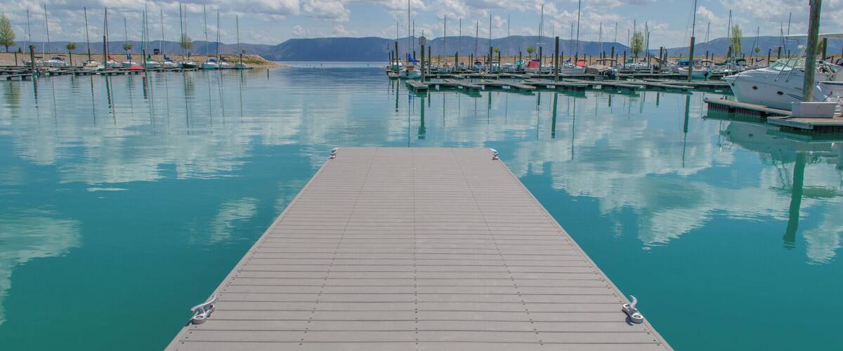 A marina with boats docked, calm water, and a clear sky.