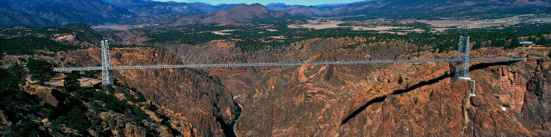 A suspension bridge spanning a deep canyon with rugged mountains in the background.