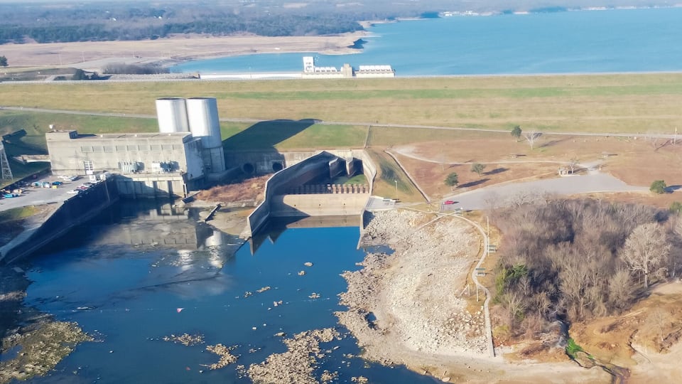 A dam, a reservoir, and a coastal area with a road and sparse vegetation.