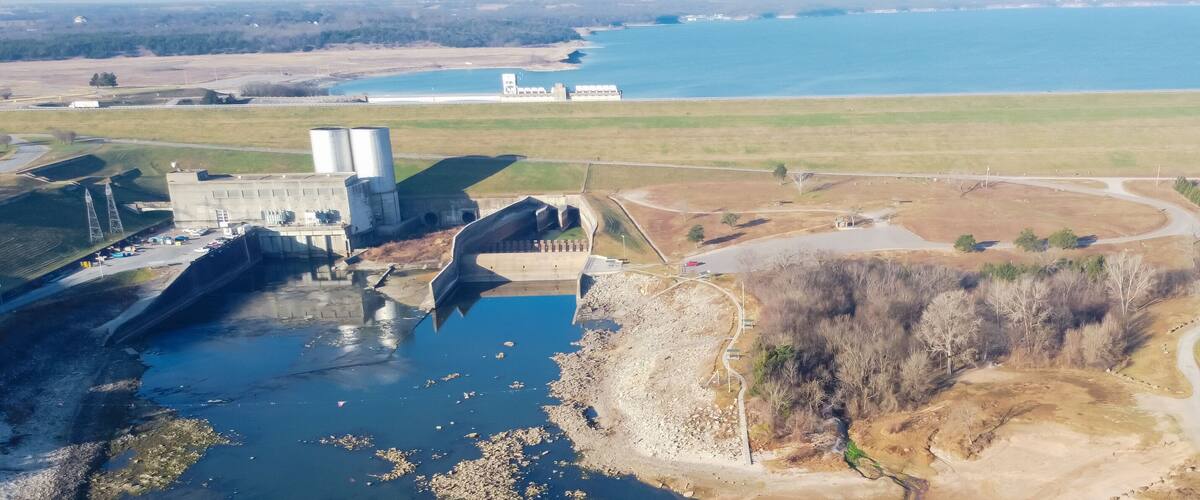 A dam, a reservoir, and a coastal area with a road and sparse vegetation.