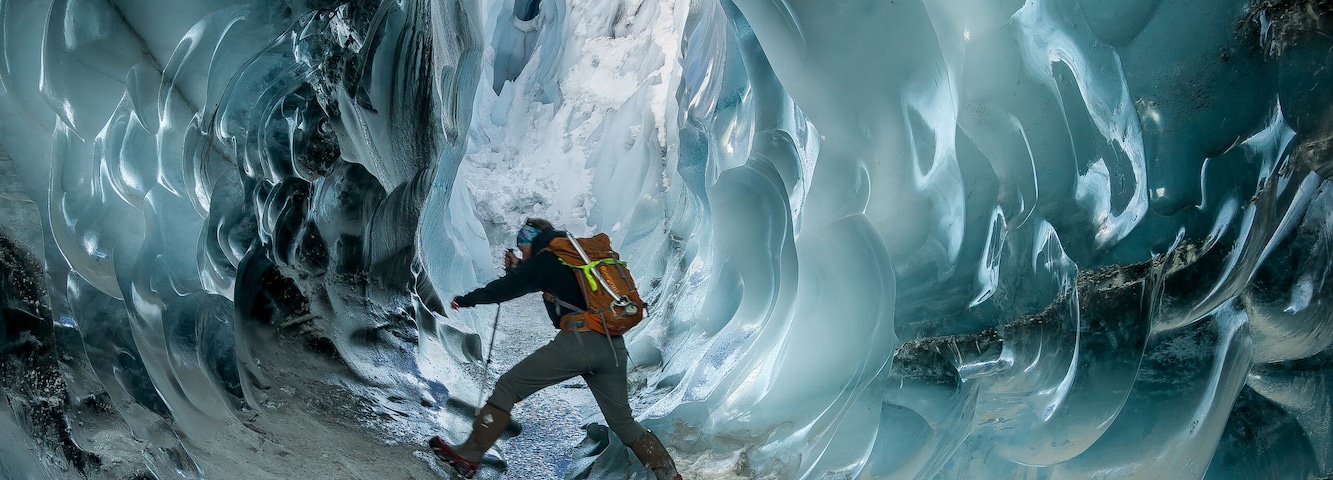 Uma pessoa dentro de uma caverna glacial com formações de gelo.