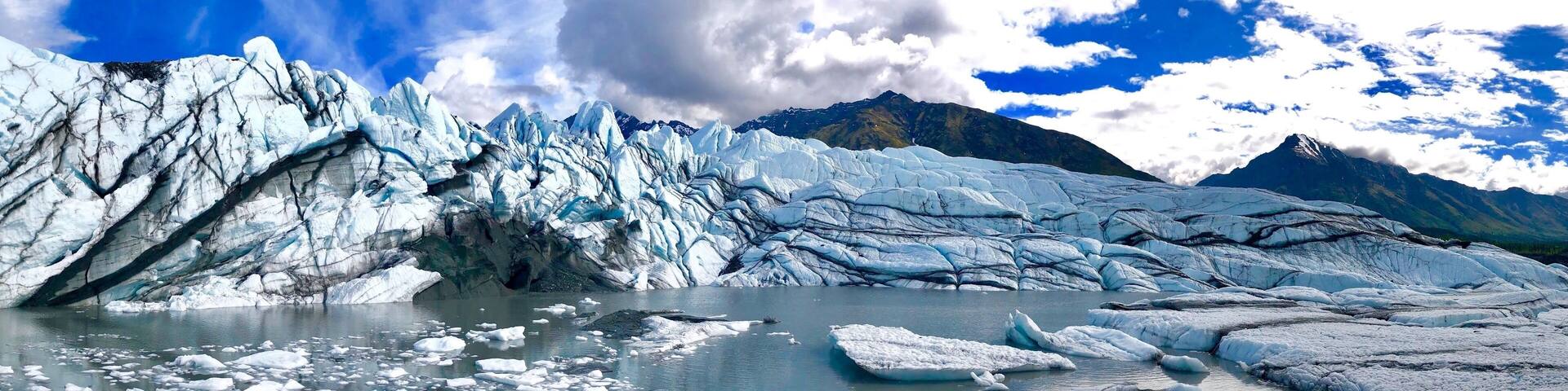 A glacier with icebergs in a body of water, surrounded by mountains.