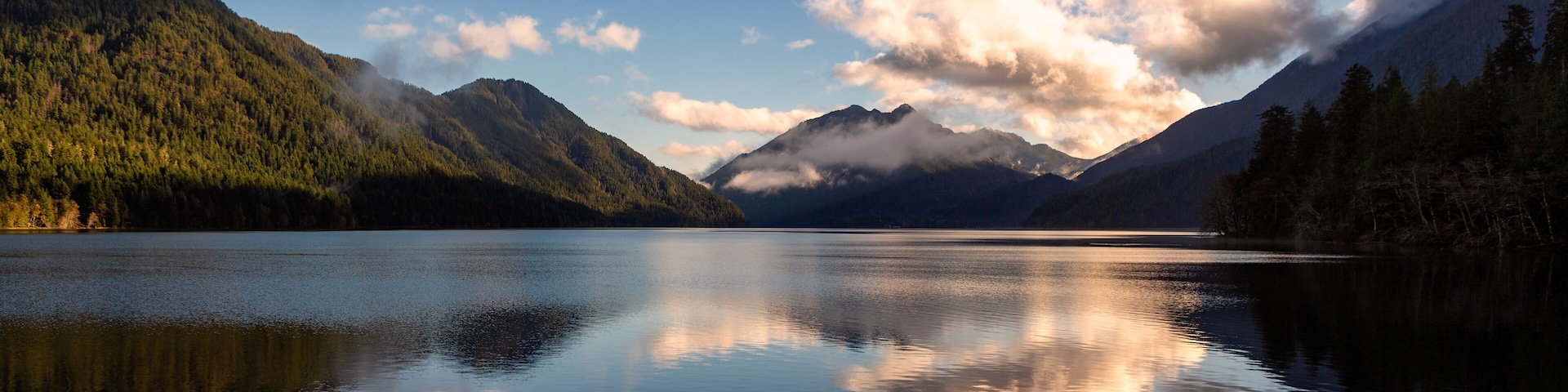 A calm lake reflecting mountains and a partly cloudy sky.