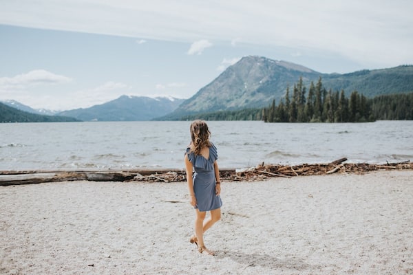 Eine Frau geht an einem Strand, im Hintergrund Berge.
