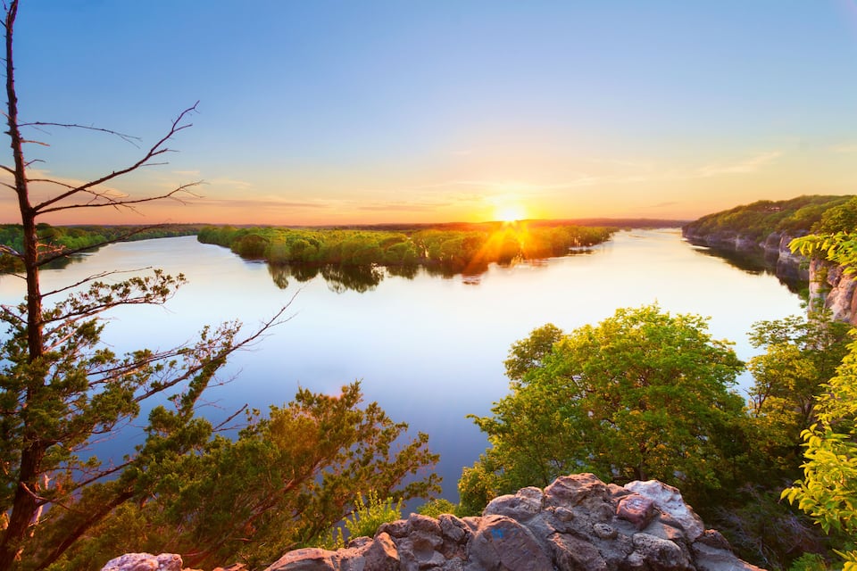A river surrounded by lush greenery and rocky cliffs during sunset.