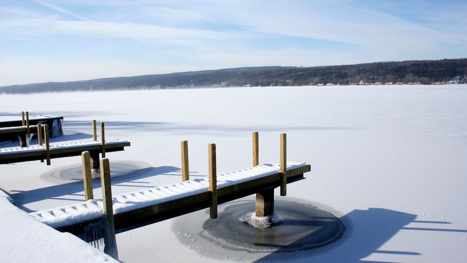 View of snow covered piers on frozen Keuka Lake in the Finger Lakes area of New York. Blue sky, clouds and opposite shore beyond.; Shutterstock ID 71665858