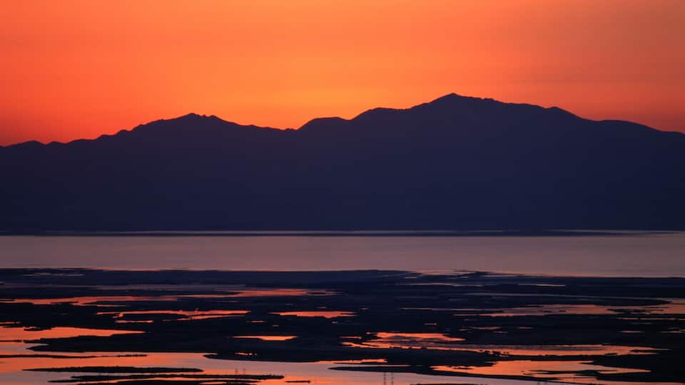 A sunset over a mountainous landscape with a body of water reflecting the sky's colors.