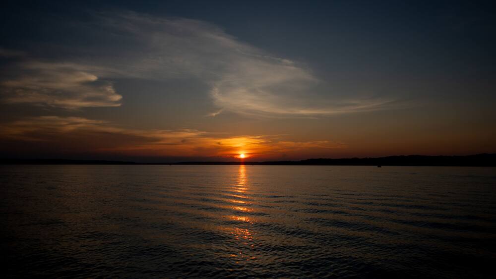 A sunset over a calm body of water with a silhouette of land in the distance.