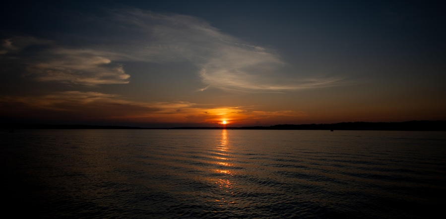 A sunset over a calm body of water with a silhouette of land in the distance.