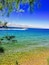 A clear blue sea with a boat, pebbly shore, and mountains in the distance.