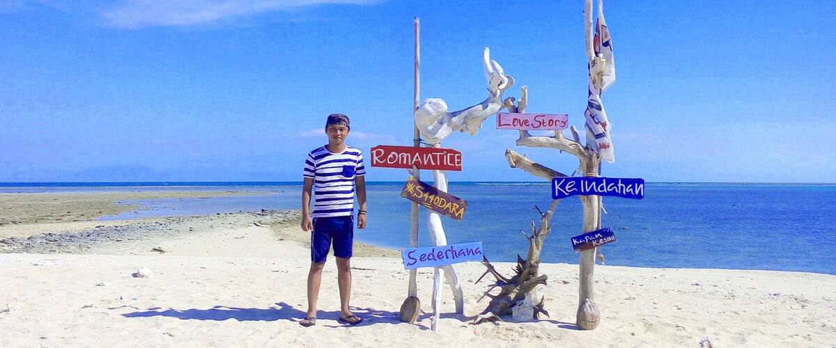 A beach with a person standing next to a signpost with multiple signs.
