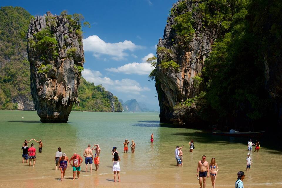 A beach with people and a boat, surrounded by rocky cliffs.