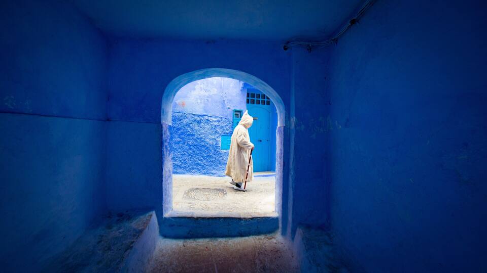 A person in a white robe walking through a blue-walled corridor with a blue door and a blue wall.