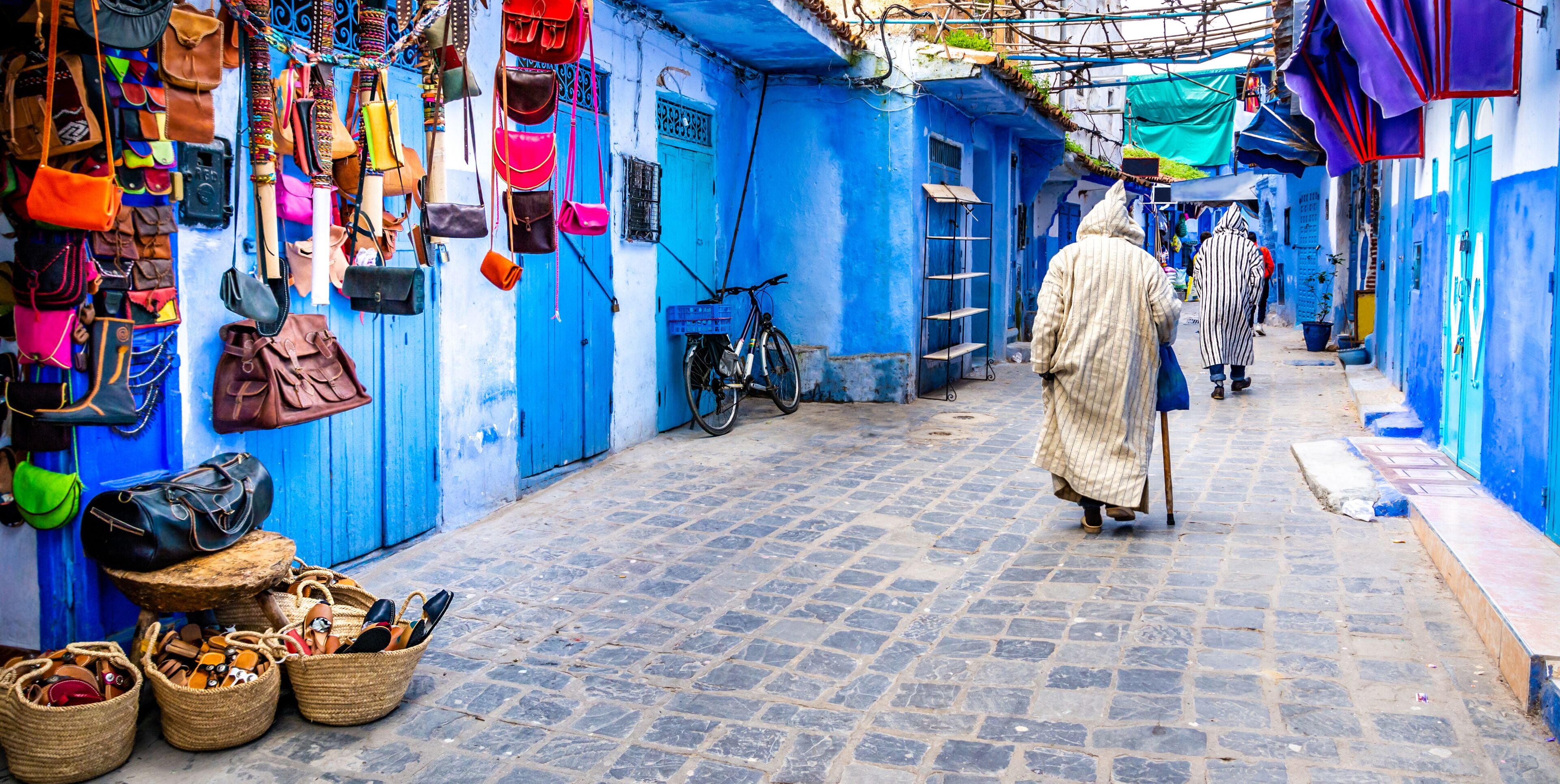 A narrow street with blue buildings, a bicycle, and various bags displayed on the walls.