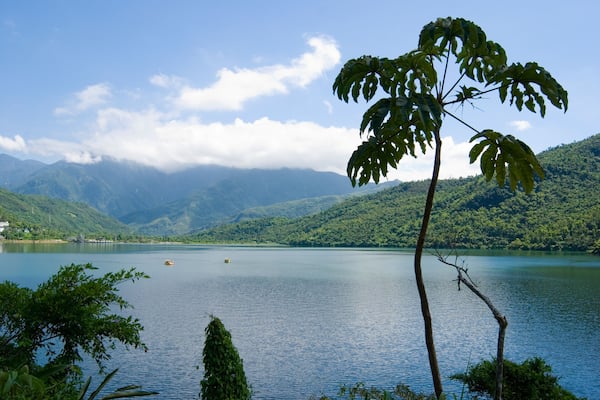 A calm lake surrounded by lush green hills and a clear sky.