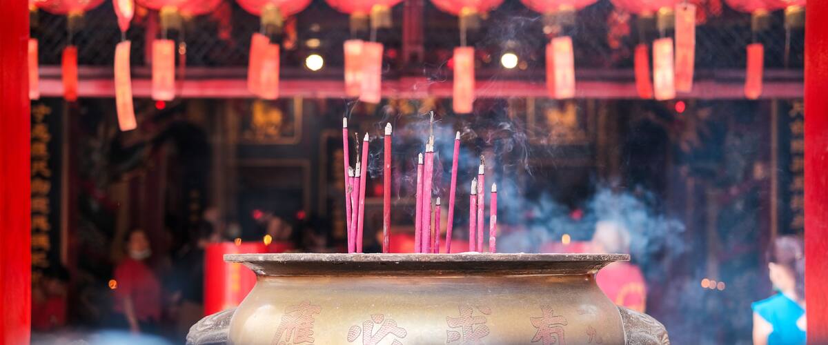 A large brass incense burner with burning sticks releases smoke in a Chinese temple at Jakarta’s Chinatown, surrounded by lanterns and traditional decorations, symbolizing prayers and blessings.