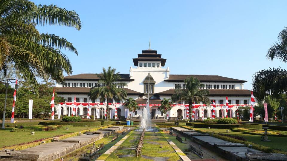 A large building with a central tower, surrounded by a well-maintained garden with a fountain.