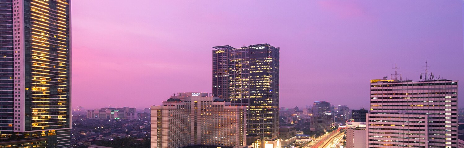 A cityscape at dusk with a circular water feature in the center, surrounded by high-rise buildings and busy roads.