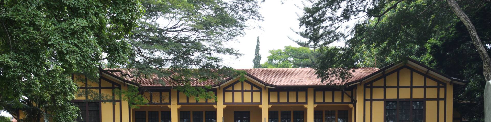 A yellow building with a tiled roof, surrounded by a well-maintained lawn and trees.