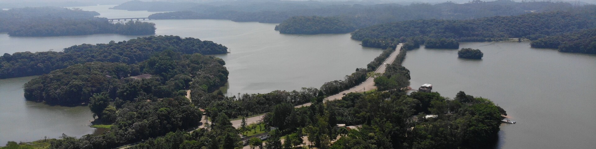 Um rio serpenteando por uma paisagem arborizada, com uma ponte e uma estrada.