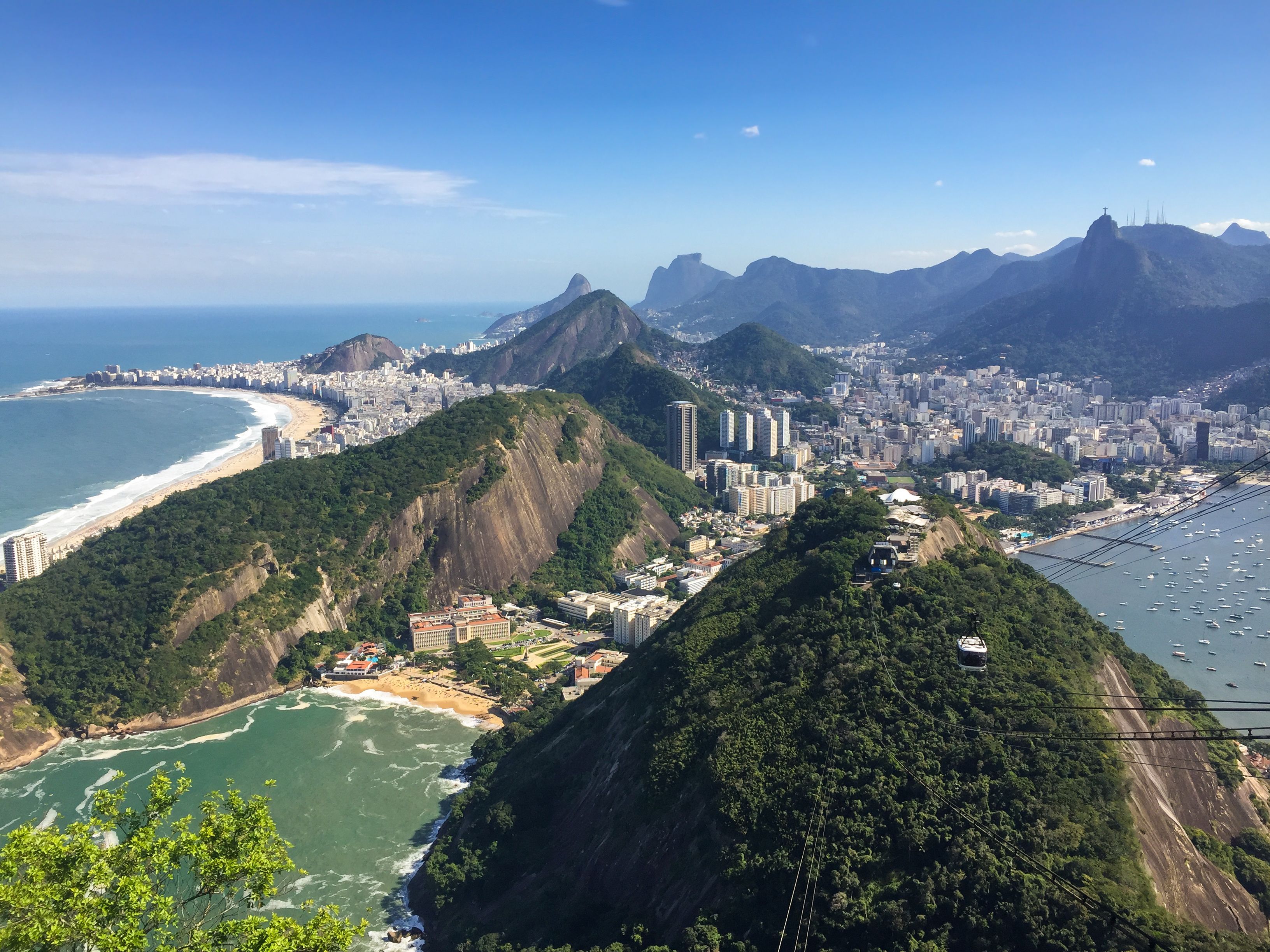 A coastal city with a prominent mountain, a beach, and a cable car line.