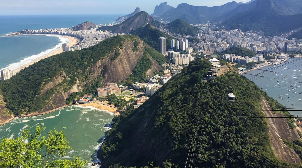 A coastal city with a prominent mountain, a beach, and a cable car line.