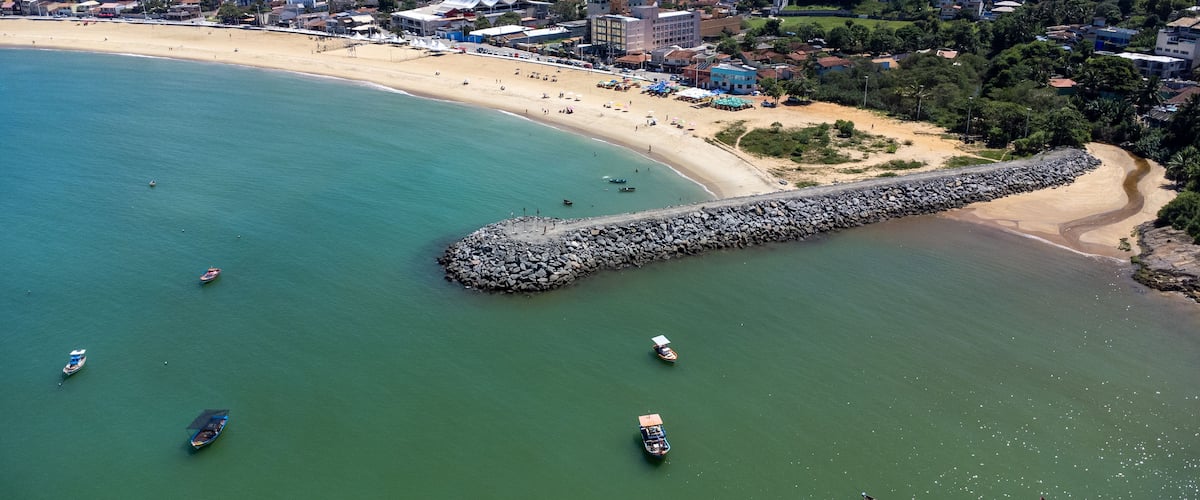 Un pueblo costero con playa, barcos y un rompeolas rocoso.