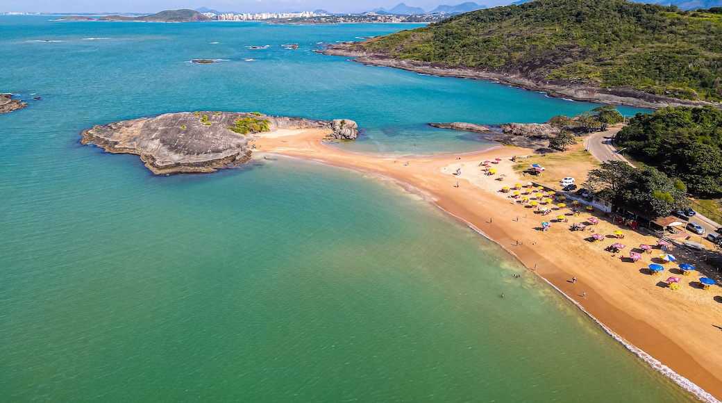 Un paisaje costero con una playa arenosa, aguas turquesas cristalinas y un promontorio rocoso.