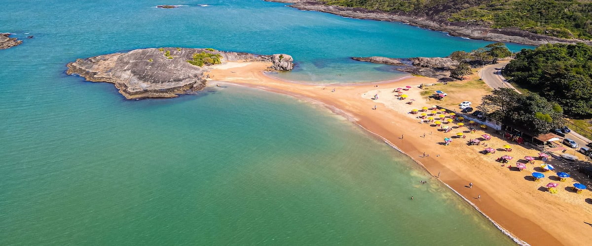 A coastal landscape with a sandy beach, clear turquoise waters, and a rocky outcrop.