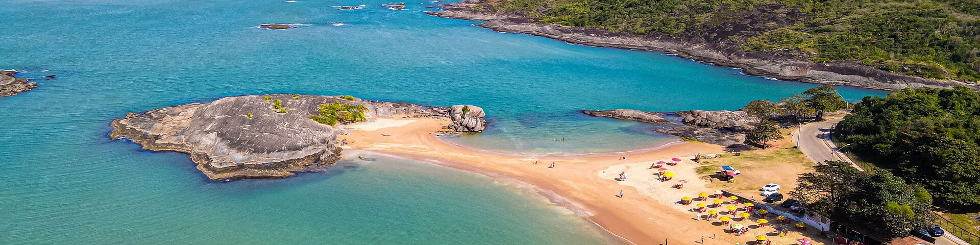 Un paisaje costero con una playa arenosa, aguas turquesas cristalinas y un promontorio rocoso.
