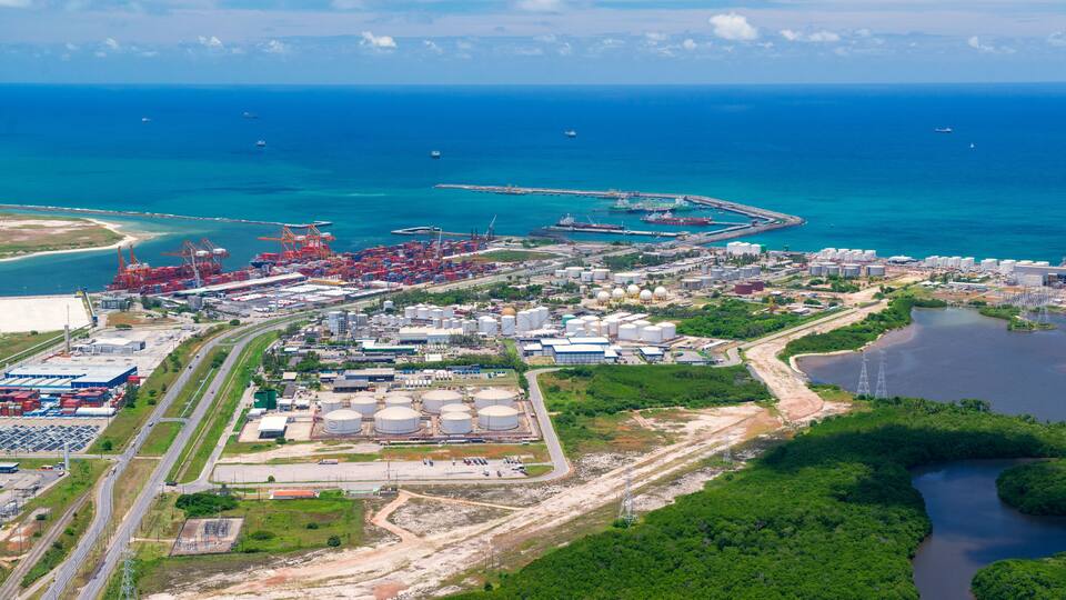 Un puerto industrial con contenedores de transporte, tanques de almacenamiento y un puerto deportivo con barcos.