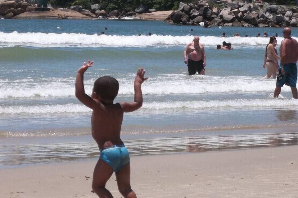 A beach with waves, people, and a lighthouse in the background.