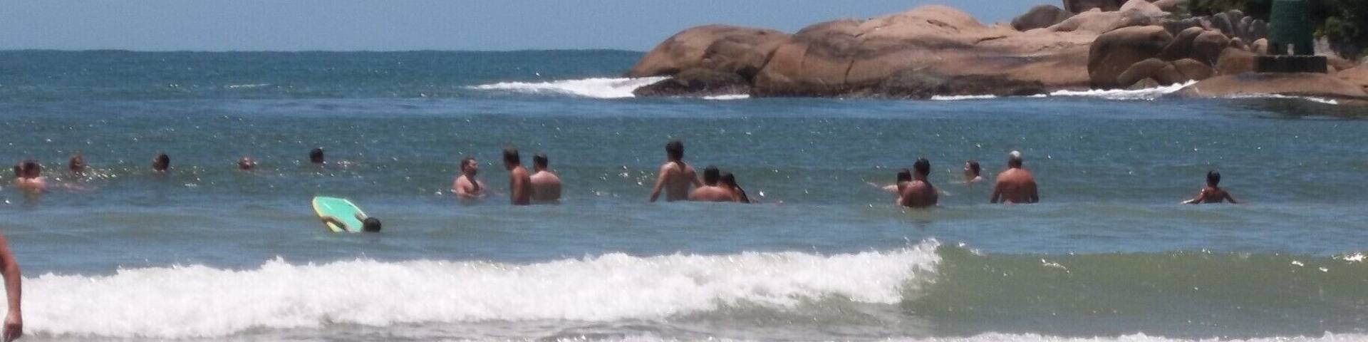 Una playa con gente nadando y practicando surf, y un niño caminando por la orilla.