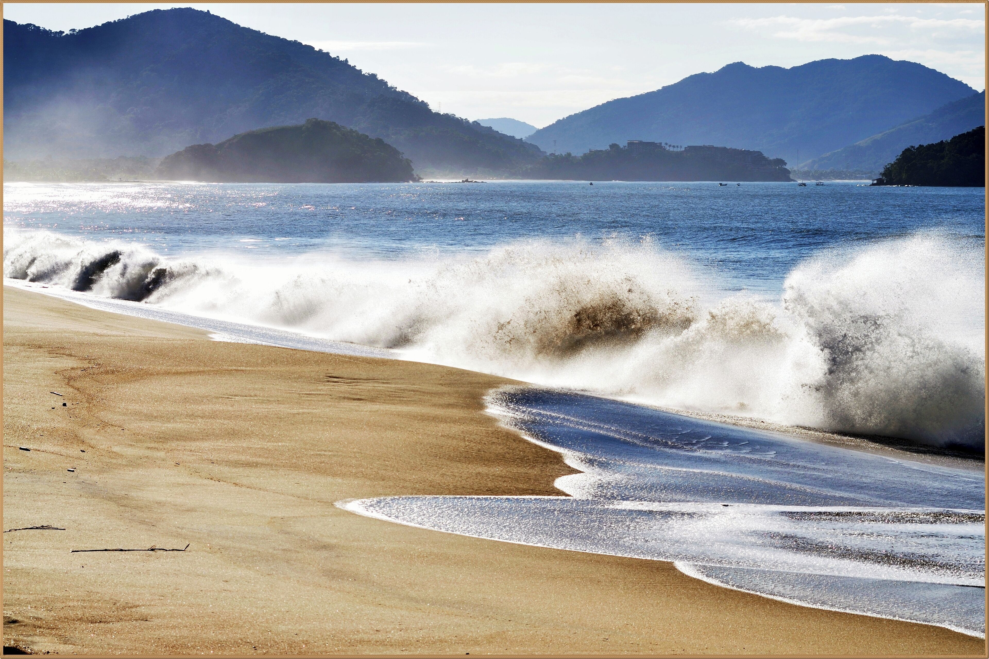 A beach with waves crashing onto the shore, surrounded by mountains.