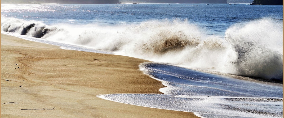 A beach with waves crashing onto the shore, surrounded by mountains.